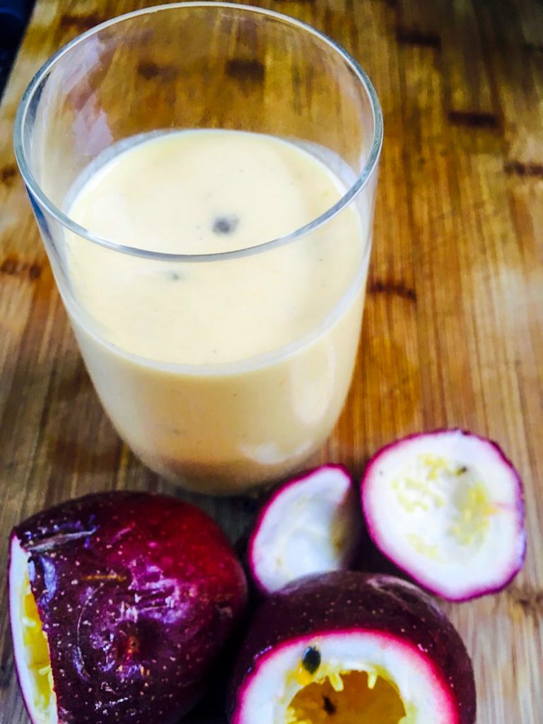 A glass of mango and passionfruit smoothie surrounded by fresh passionfruit